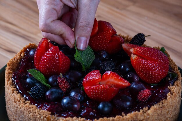 Foto mãos femininas decorando uma torta de bagas com frutas