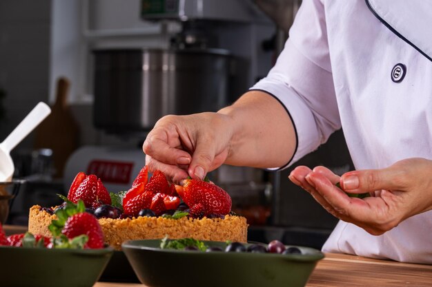 Foto mãos femininas decorando uma torta de bagas com frutas