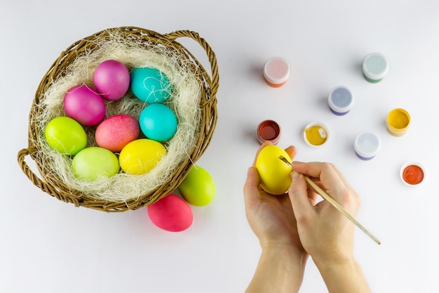 Mãos femininas desenhando um ovo de Páscoa com uma cesta cheia de ovos pintados multicoloridos