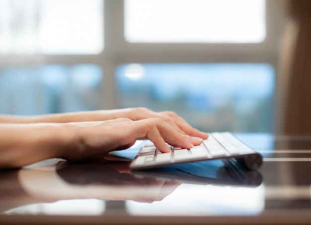 Mãos femininas digitando texto no teclado enquanto trocam mensagens com amigos através de redes sociais usando um laptop de computador. Uma trabalhadora de escritório verifica seu e-mail enquanto está sentada em uma mesa.