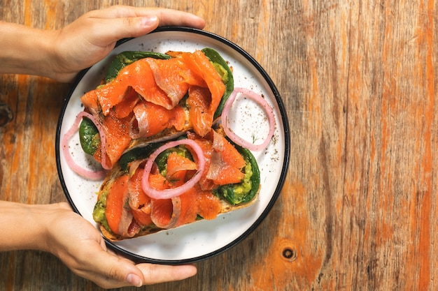 Mãos femininas e deliciosas torradas com folhas de salmão defumado, abacate e manjericão