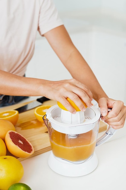 Mãos femininas e espremedor de frutas cítricas durante a preparação de suco de laranja fresco