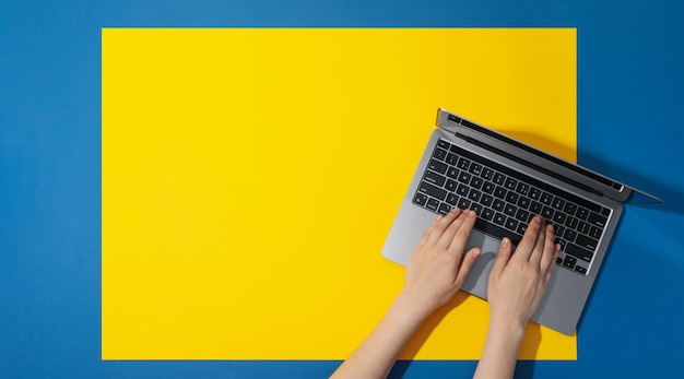 Mãos femininas e laptop em fundo azul amarelo