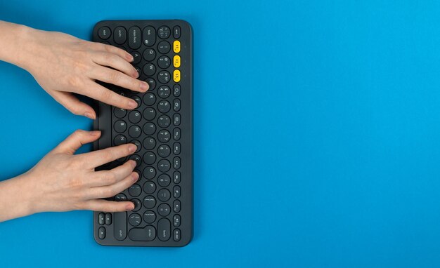 Mãos femininas e teclado em um fundo azul Conceito de trabalho no espaço de trabalho no computador doméstico e design freelance Vista superior plana e foto do espaço de cópia