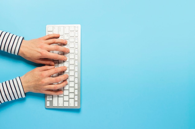 Mãos femininas e teclado sobre um fundo azul. Espaço de trabalho do conceito, trabalho no computador, freelance, design.