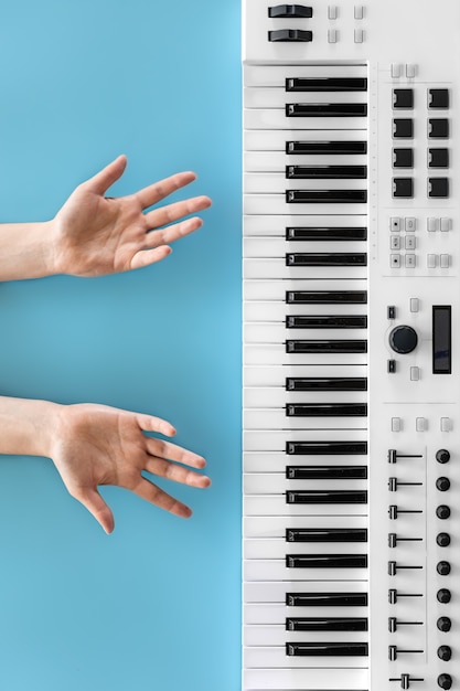 Foto mãos femininas e teclas musicais em um fundo azul, o conceito de educação, uma pessoa não pode tocar piano.