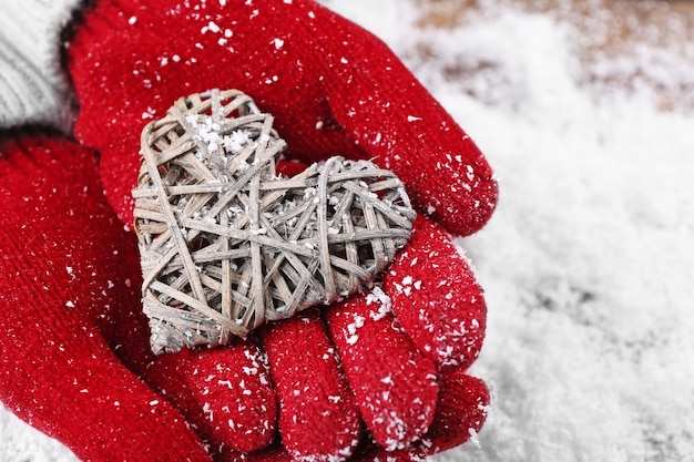 Mãos femininas em luvas com coração decorativo em fundo de neve