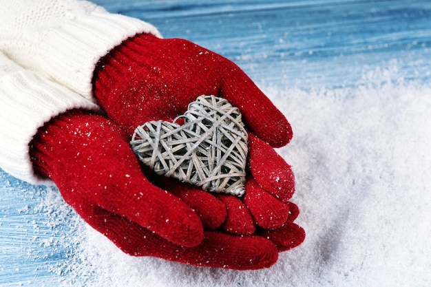 Mãos femininas em luvas com coração decorativo em fundo de neve