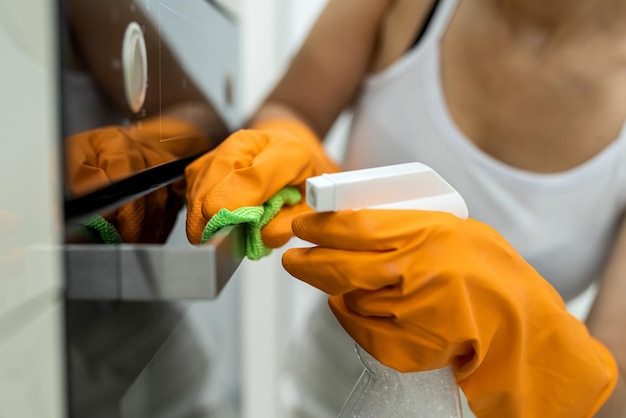 Foto mãos femininas em luvas com um frasco de detergente para limpar o forno da cozinha