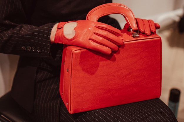 Mãos femininas em luvas de couro segurando uma bolsa clássica de moda vermelha brilhante