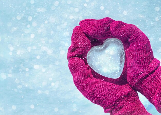 Mãos femininas em luvas de malha com coração de gelo no dia de inverno Conceito de amor