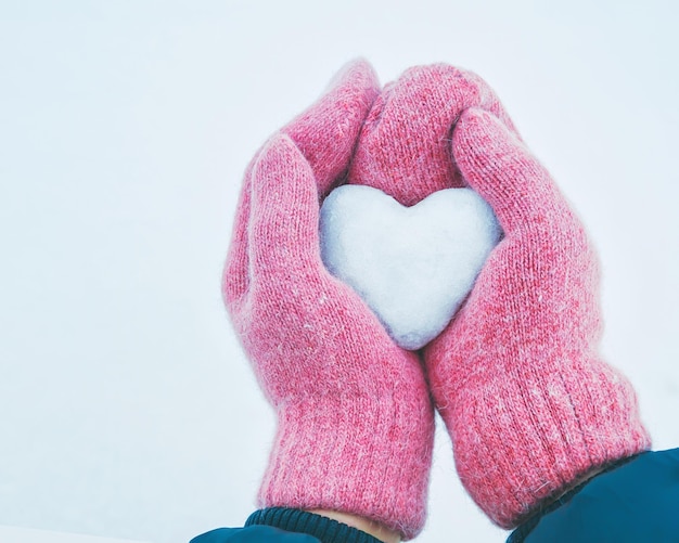 Foto mãos femininas em luvas de malha com coração de neve em dia de inverno. conceito de amor. dia dos namorados backgr