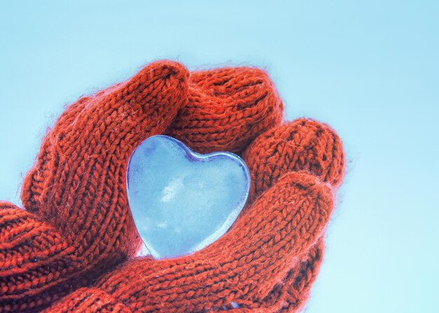 mãos femininas em luvas de malha com coração de neve em dia de inverno. Conceito de amor.