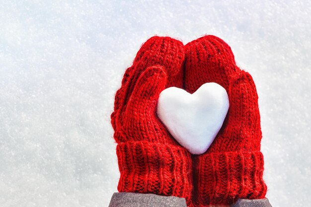Mãos femininas em luvas de malha com coração de neve no dia de inverno Conceito de amor