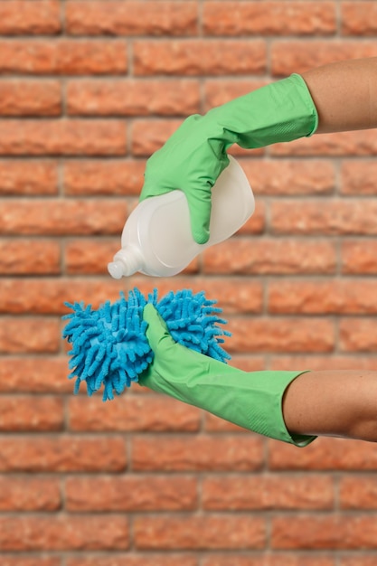 Mãos femininas em luvas de proteção com garrafa de detergente