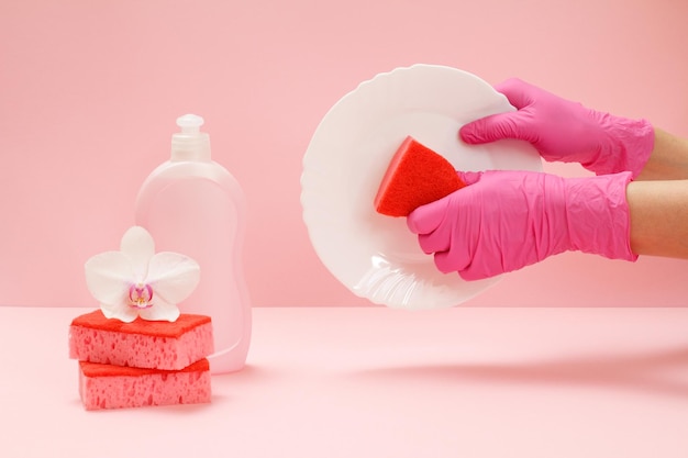 Mãos femininas em luvas de proteção com placa e esponja uma garrafa de esponjas líquidas para lavar louça