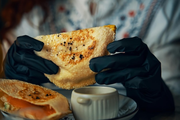 Mãos femininas em luvas pretas estão segurando um prato tradicional de sanduíche de pitas de pão de milho com peixe e...