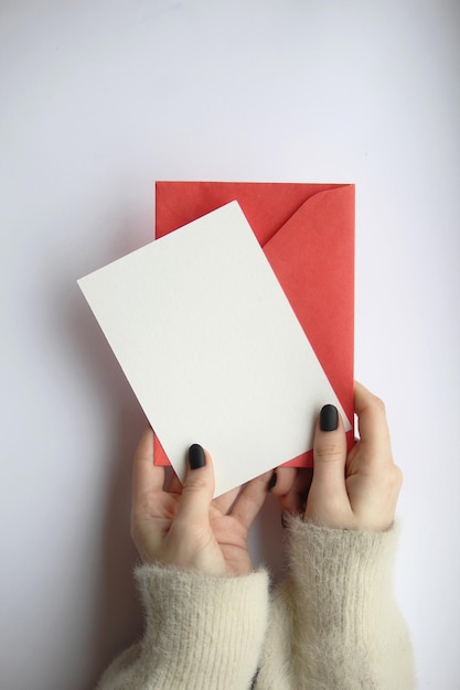 mãos femininas em um suéter com manicure segurando uma folha branca e um envelope vermelho em um layout de cartão postal de fundo branco