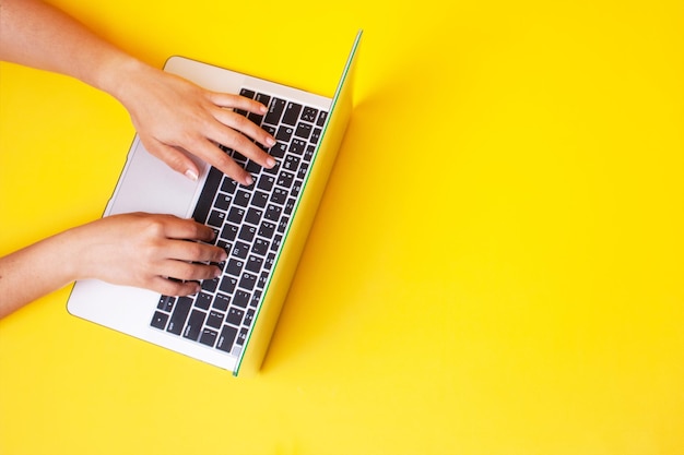 Mãos femininas em um teclado de laptop em um fundo amarelo. trabalhe remotamente como freelance. espaço vazio