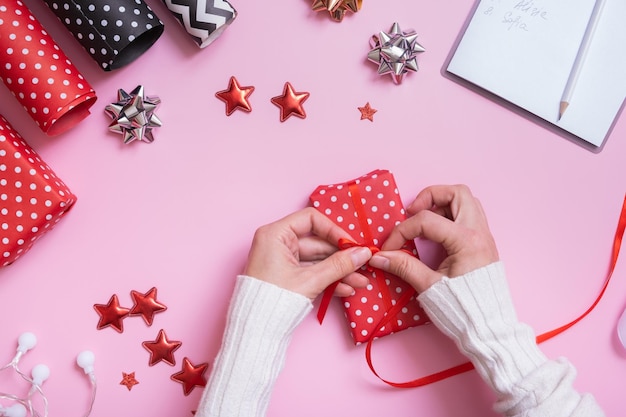 Mãos femininas embrulhando presentes de natal em plano de fundo rosa Vista superior preparação de natal