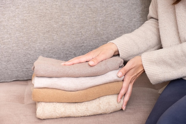 Mãos femininas empilham suéteres de malha aconchegantes no sofá Conceito quente