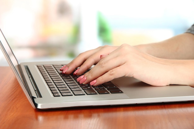 Mãos femininas escrevendo no laptop em fundo brilhante