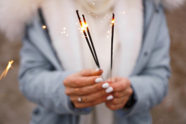 Mãos femininas estão segurando estrelinhas acesas. Mulher ao ar livre no inverno. Fundo desfocado