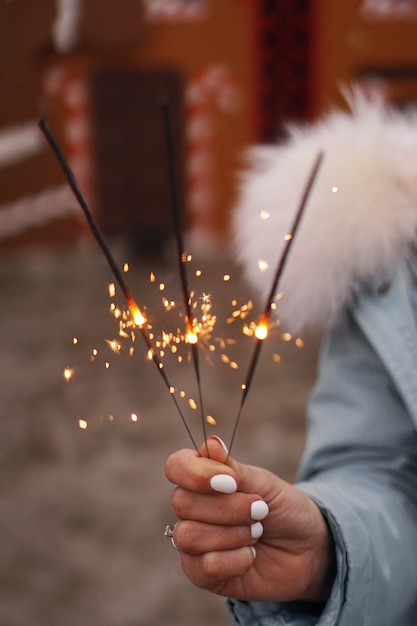 Mãos femininas estão segurando estrelinhas acesas. Mulher ao ar livre no inverno. Fundo desfocado