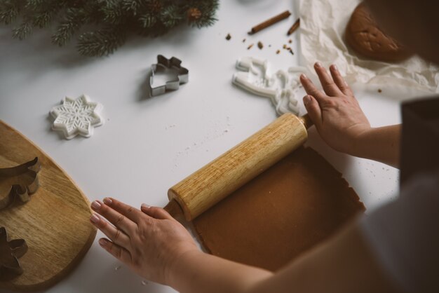 Mãos femininas estendem a massa de gengibre cru com um rolo sobre uma mesa branca