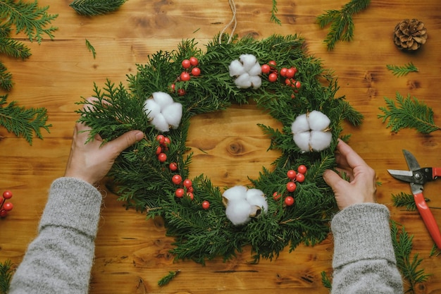 Mãos femininas fazendo guirlanda de natal diy decoração de casa de inverno