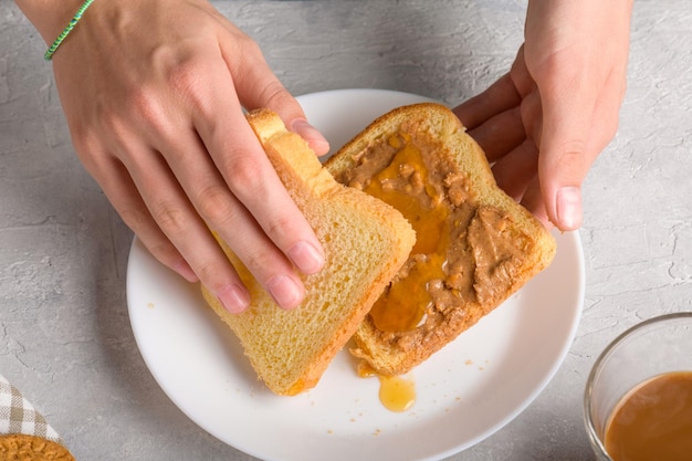 Foto mãos femininas fazendo um sanduíche com mel e manteiga de amendoim espalhando em um pedaço de pão branco