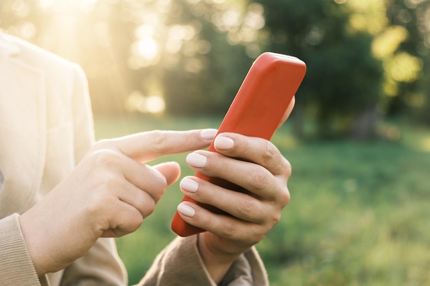 Mãos femininas fechadas usando o fundo da natureza do smartphone Mulher pessoa telefone celular pôr do sol ao ar livre