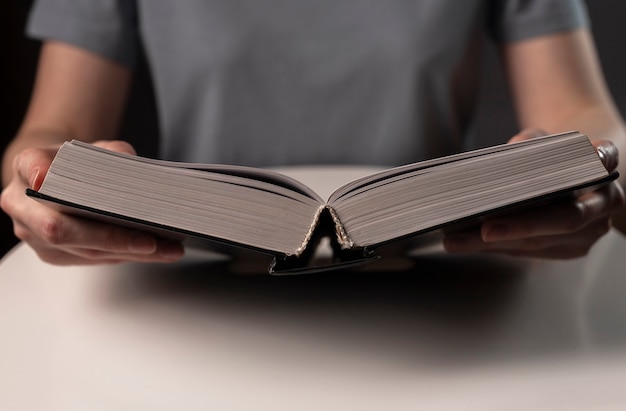 Mãos femininas fechem, segurando e lendo um livro ou livro-texto em capa dura à noite.