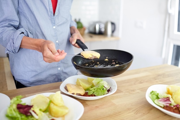 Mãos femininas frigideira preta batatas cozidas salada verde carne costeleta prato de queijo na mesa de madeira