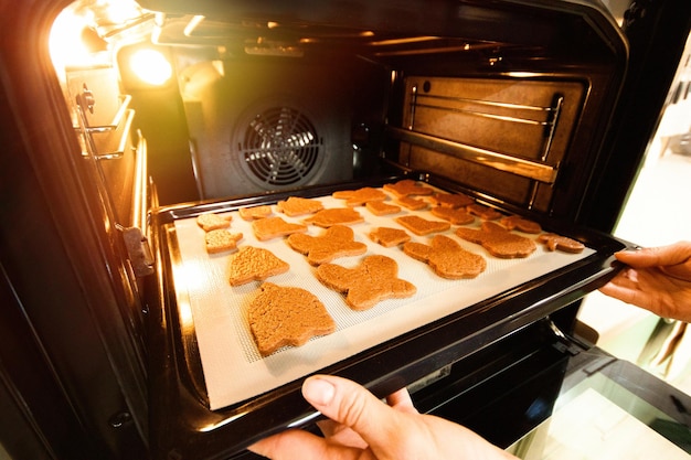 Mãos femininas inserem uma assadeira com biscoitos no forno