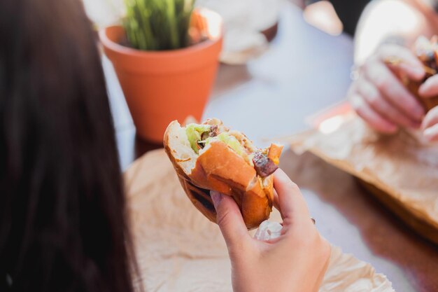 Mãos femininas jovens estão segurando um hambúrguer mordido em um restaurante de fast food