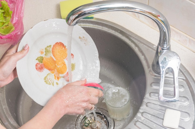 Mãos femininas lavam os pratos Trabalho de casa na cozinha Criação de limpeza e ordem