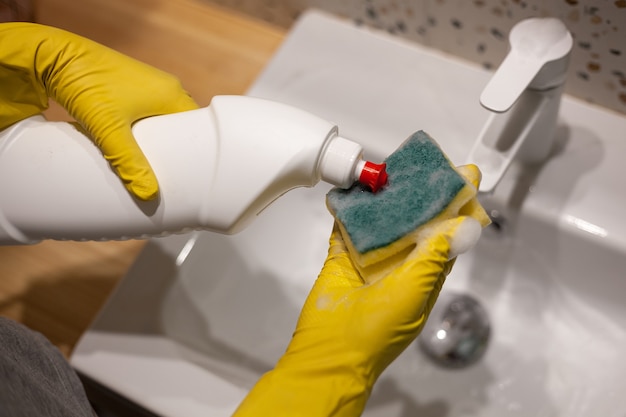 Mãos femininas limpando banheiro lavando pia com luvas de proteção em casa
