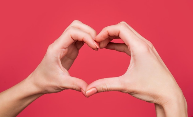 Mãos femininas mostrando gesto de coração de amor em fundo vermelho