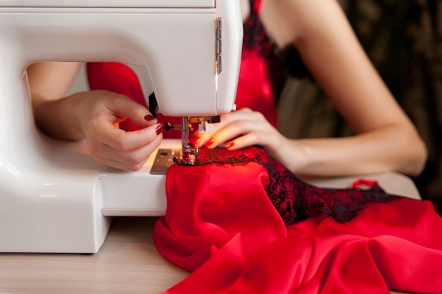 Mãos femininas na máquina de costura. processo de fabricação de lingerie de seda. feche acima do trabalho da costureira.