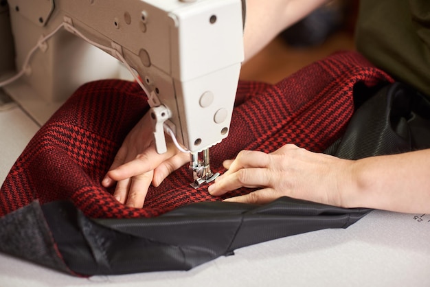 Mãos femininas no processo de costura e reparação de tecido xadrez na máquina de fabricação profissional Close up view