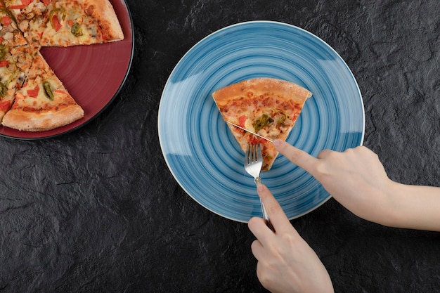 Mãos femininas pegando uma fatia de pizza do prato em fundo preto.