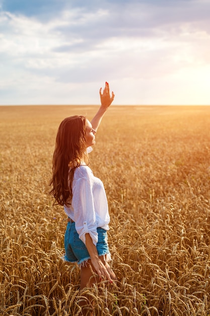 Mãos femininas se projetam do campo de trigo, jovem feliz é livre em um campo de trigo dourado maduro n ...