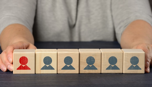 Mãos femininas seguram cubos de madeira com estatuetas. Conceito de pesquisa de funcionários, recrutamento de pessoal. Seleção de funcionários talentosos e únicos para o avanço na carreira