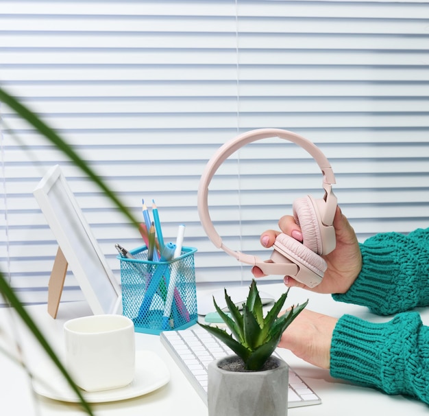 Mãos femininas seguram fones de ouvido sem fio rosa, um homem se senta em uma mesa com um teclado