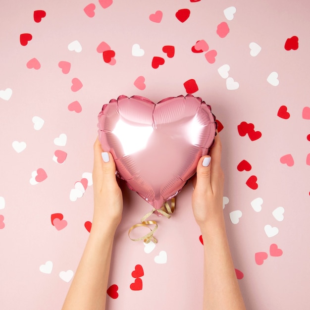 Mãos femininas seguram um balão de folha em forma de coração em fundo rosa pastel. Conceito de amor. Celebração do feriado. Decoração de Dia dos Namorados ou casamento / despedida de solteira. Balão metálico