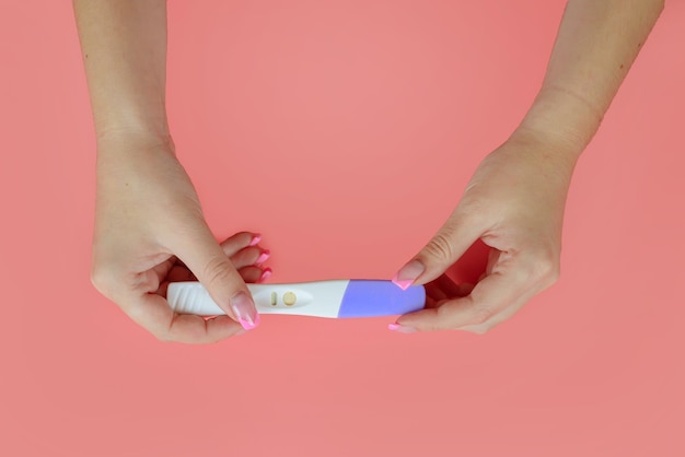 Mãos femininas seguram um teste de gravidez em um fundo rosa