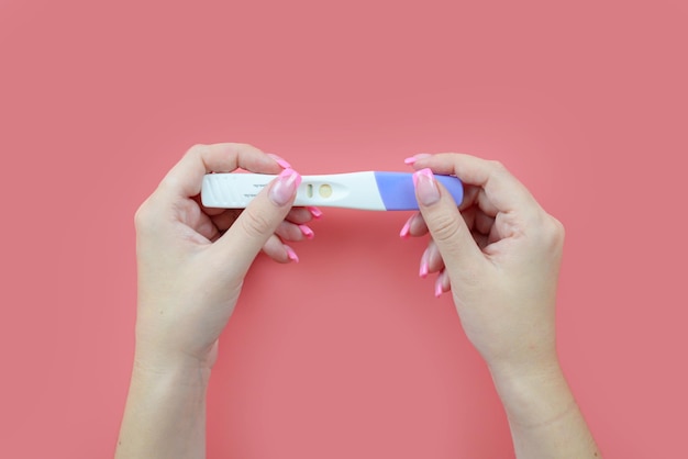 Mãos femininas seguram um teste de gravidez em um fundo rosa