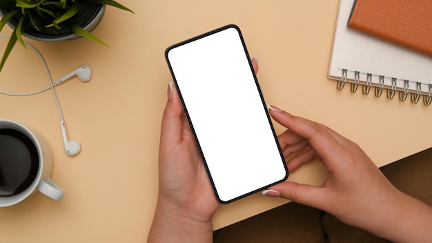 Mãos femininas segurando a tela em branco do smartphone sobre o fundo da mesa de escritório bege Mulher usa celular