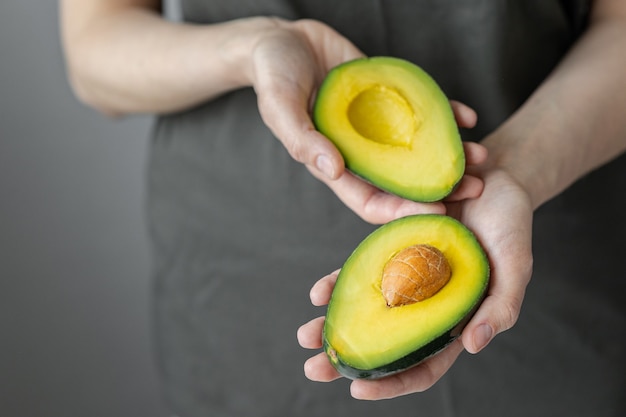 Mãos femininas segurando abacate, mulher caucasiana em camiseta escura, cozinha, chef de cozinha, abacate maduro e delicioso, comida saudável e saudável, frutas e vegetais crus vegan vegetariano